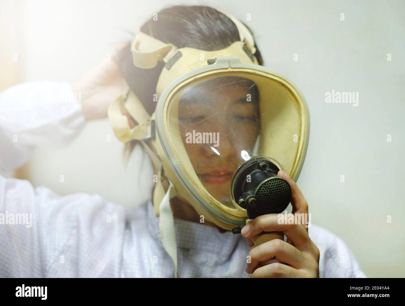Una mujer asiática que tira de una máscara de oxígeno protector de cara completa, abrigo blanco y guantes de goma, preparándose para trabajar en un laboratorio bioquímico. Foto de stock