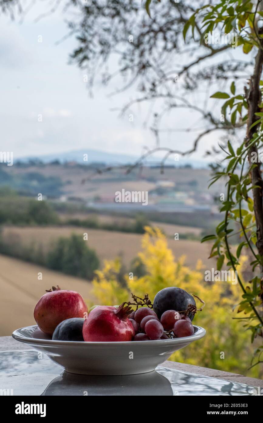 Cuenco de fruta en primer plano, las colinas italianas y el paisaje de Umbría, Tusany en el fondo. Entretener desde una Villa en Italia. Foto de stock