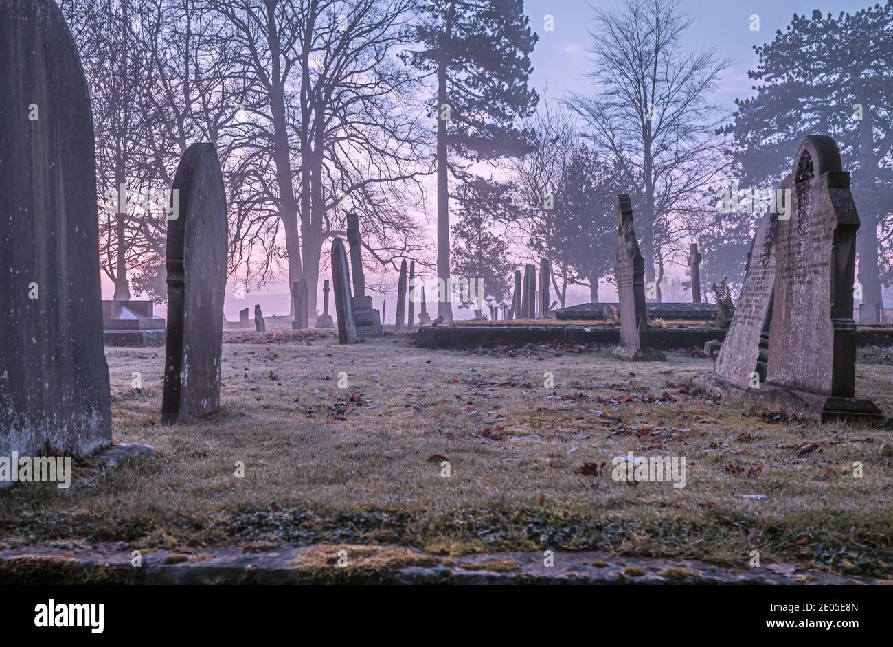 Una imagen solemne de lápidas en un patio de la iglesia en una mañana de mal humor. Foto de stock