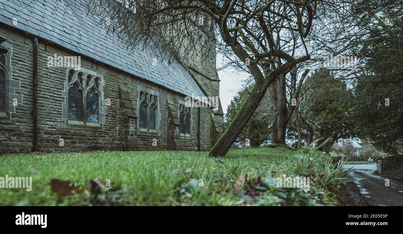 Gran angular de una iglesia brumosa y lápidas en una fría mañana de invierno al amanecer. Foto de stock