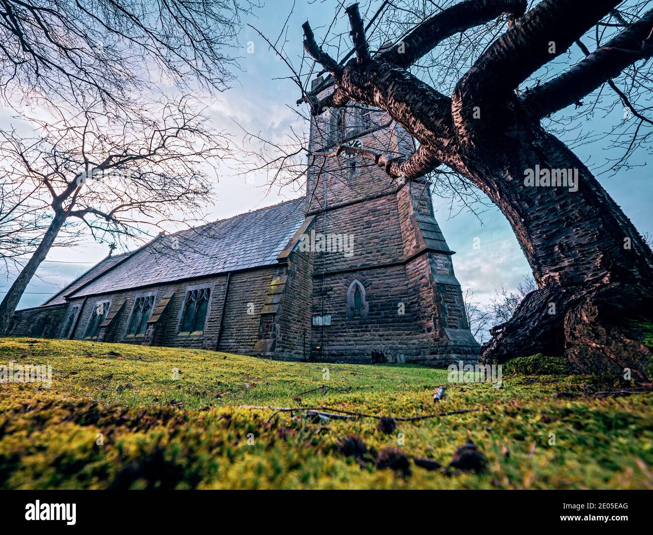 Gran angular de una iglesia brumosa y lápidas en una fría mañana de invierno al amanecer. Foto de stock