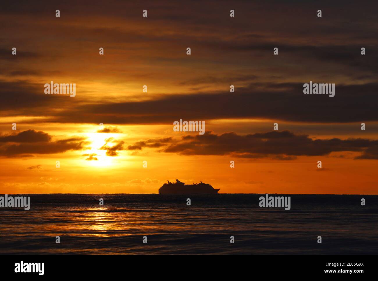 Un crucero se perfila en el horizonte contra un cielo de invierno por la mañana lleno del cálido color dorado del sol naciente que brotan a través de las nubes. Foto de stock