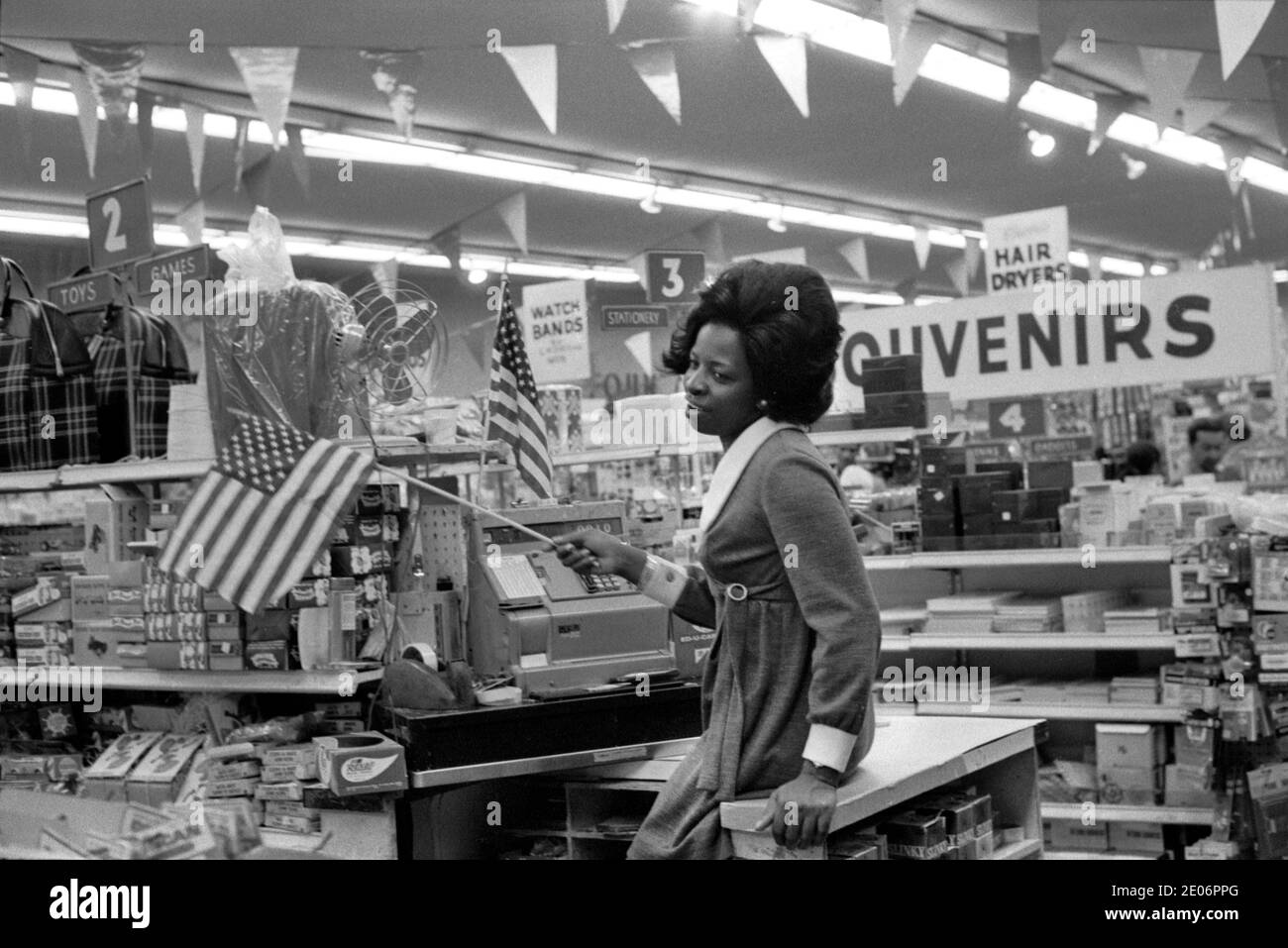 Mujer joven afroamericana que ondea la bandera de las estrellas y las rayas ella está trabajando en un centro de Manhattan Nueva York tienda de departamentos 1972. 1970 EE.UU. HOMER SYKES Foto de stock
