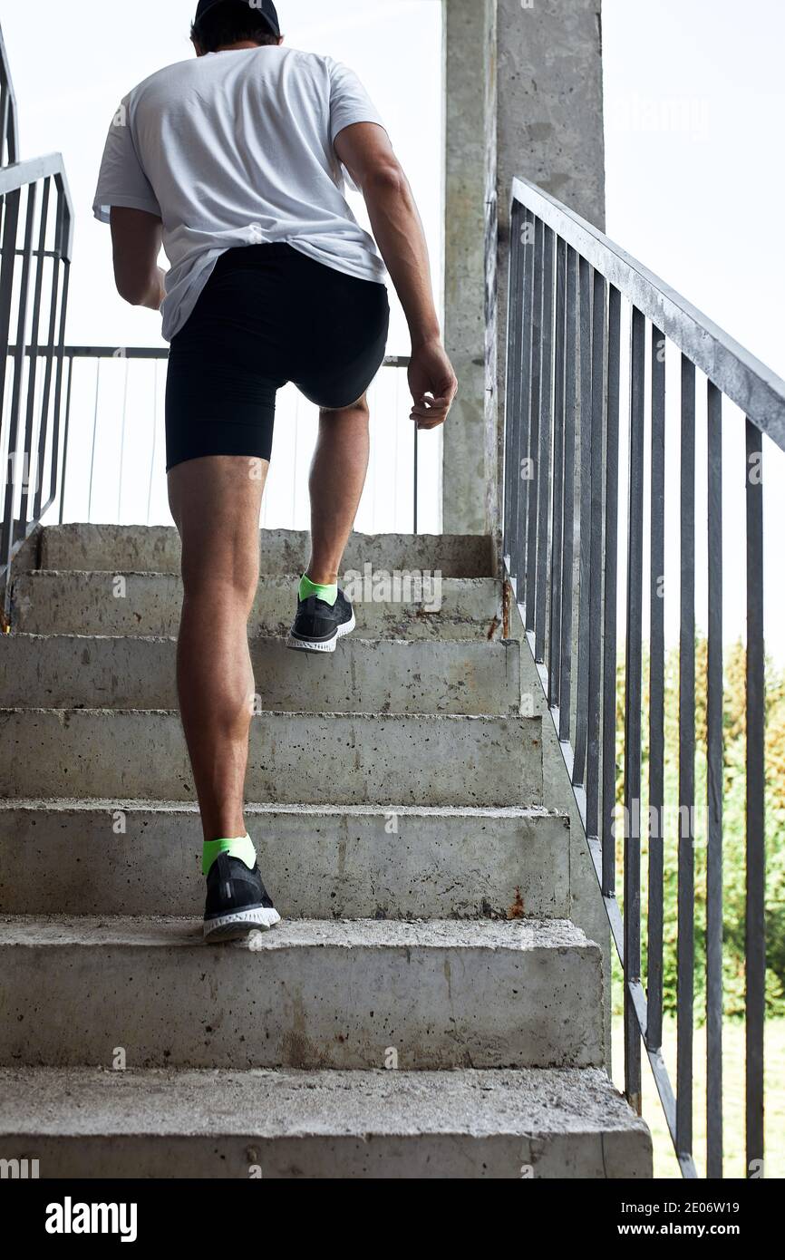 Atleta masculino concentrado corriendo por las escaleras para hacer el entrenamiento más intensivo. Deportivo hermoso joven hombre entrenando solo al aire libre. Escalera de entrenamiento conc Foto de stock