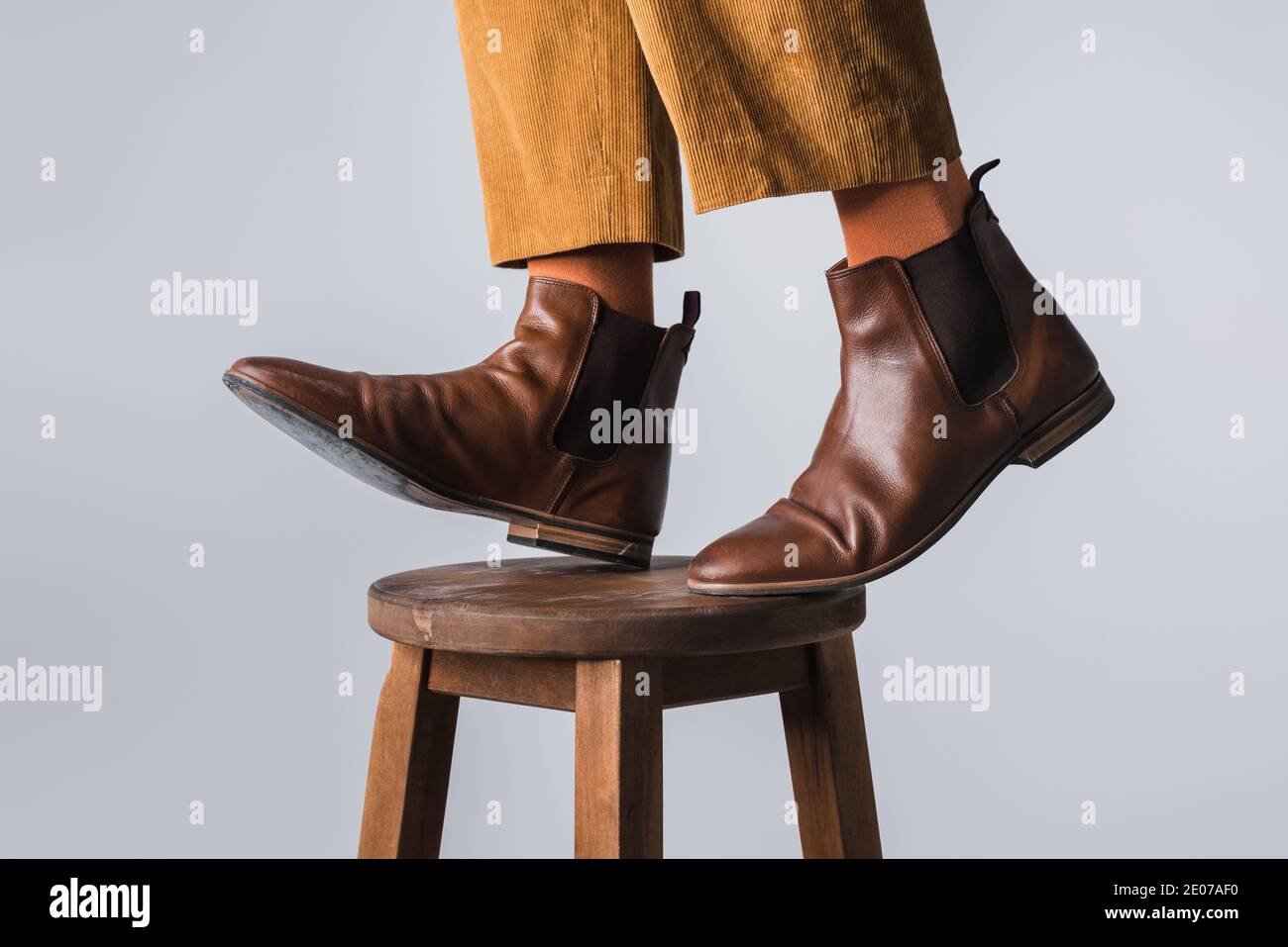 Vista recortada del hombre en calcetines naranjas y zapatos marrones de pie en silla aislada en gris Foto de stock