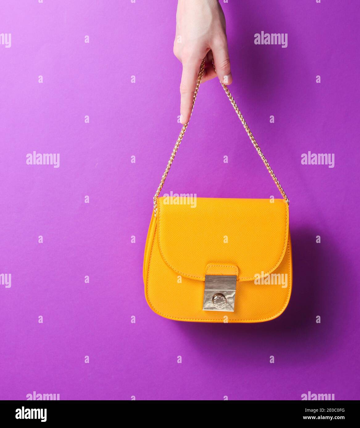 Mujer mano sostener bolsa de cuero amarillo de moda con cadena dorada sobre  fondo púrpura Fotografía de stock - Alamy