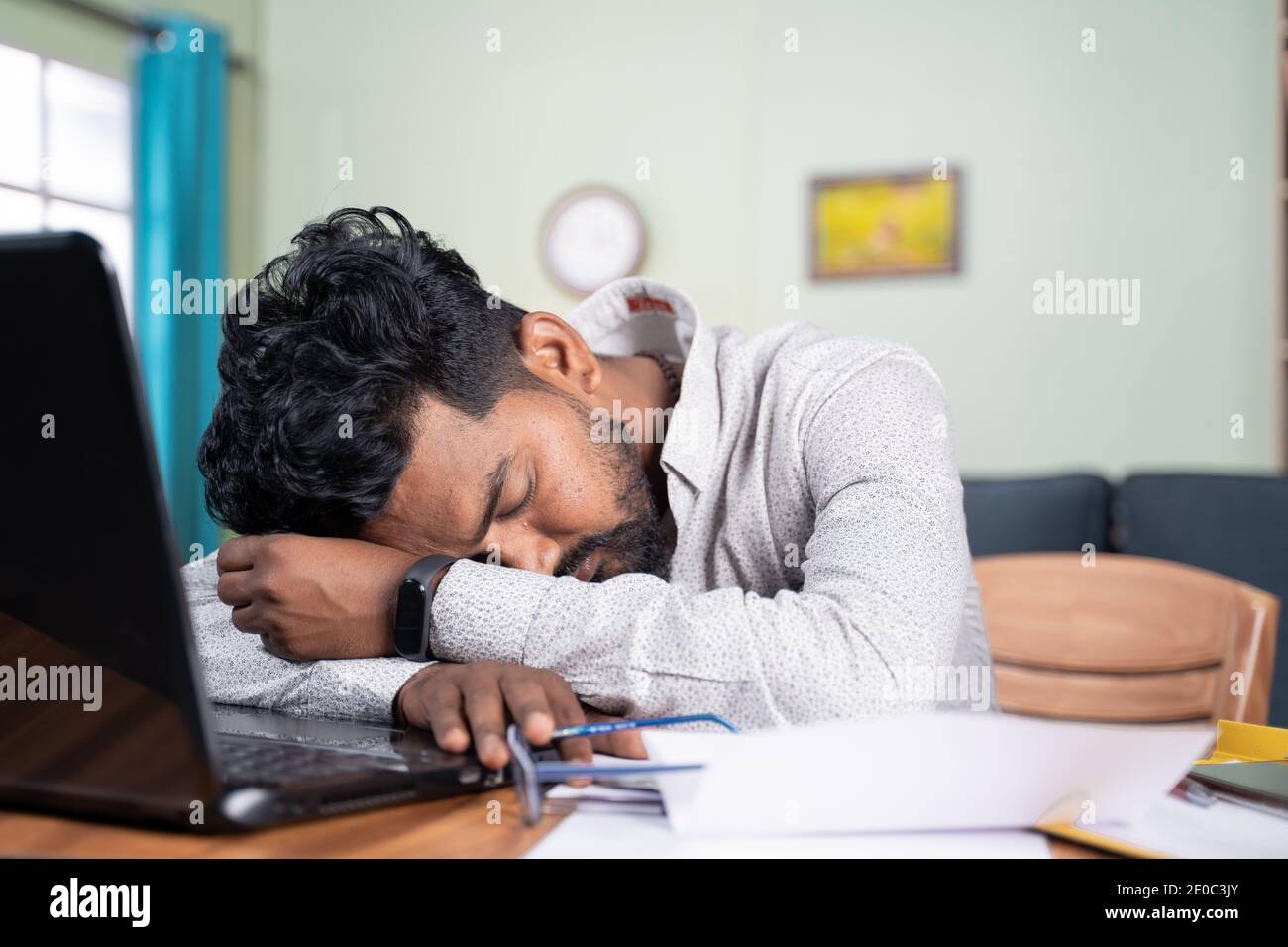 El joven se cansó de trabajar y dormía en el escritorio - agotada milenial quedarse dormido después de leer en el ordenador portátil - concepto de siesta en el lugar de trabajo Foto de stock