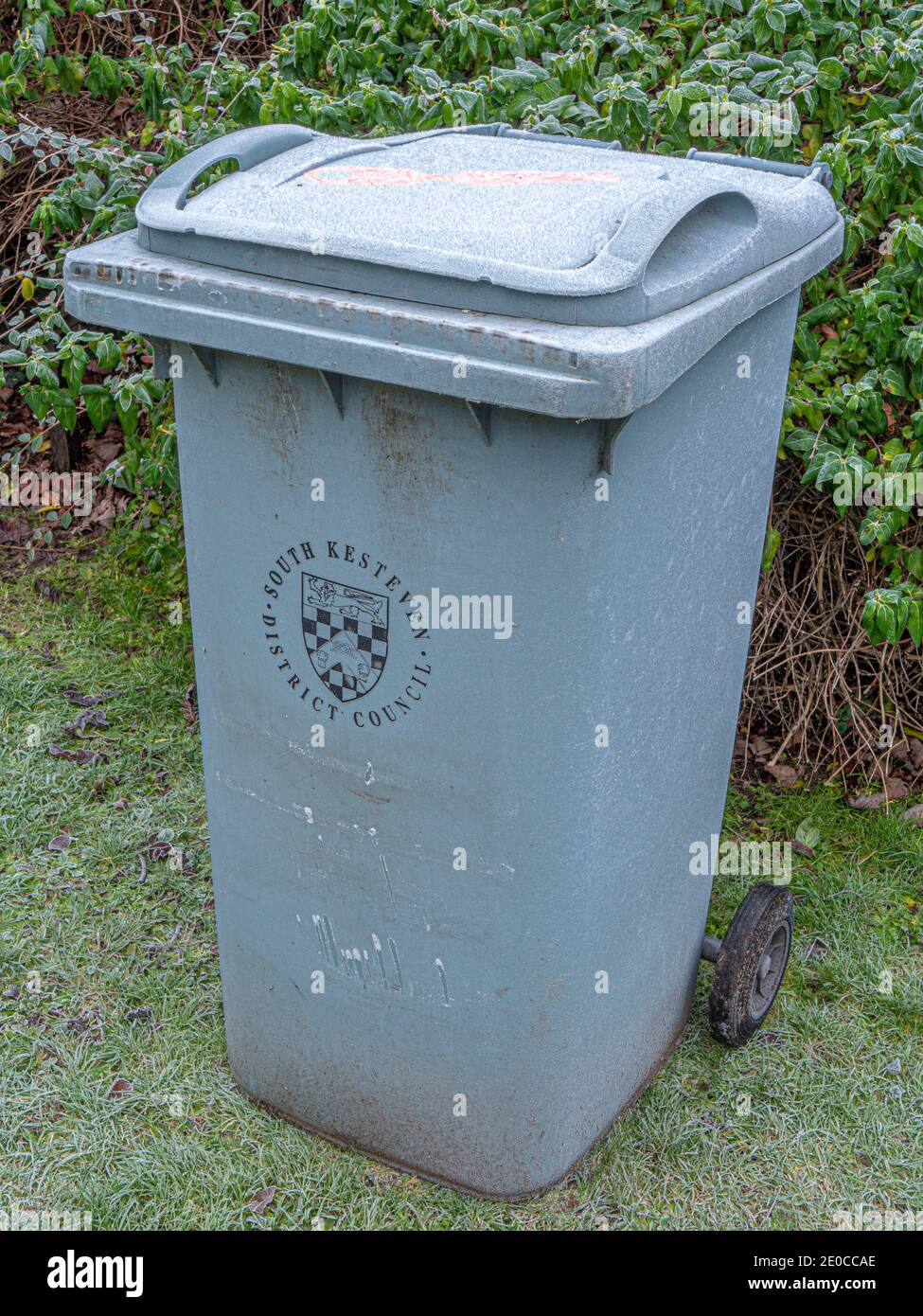 Un cubo de basura gris del consejo que se encuentra en un jardín inglés en  un frío día de invierno, con la tapa del cubo de basura cubierta de  escarcha Fotografía de