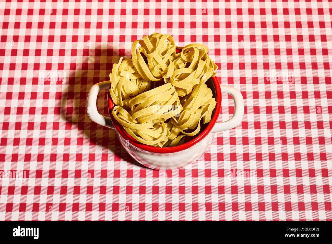 Desde arriba de deliciosos nidos de pasta fettuccine sin cocinar colocados en cacerola en mantel a cuadros en la cocina Foto de stock