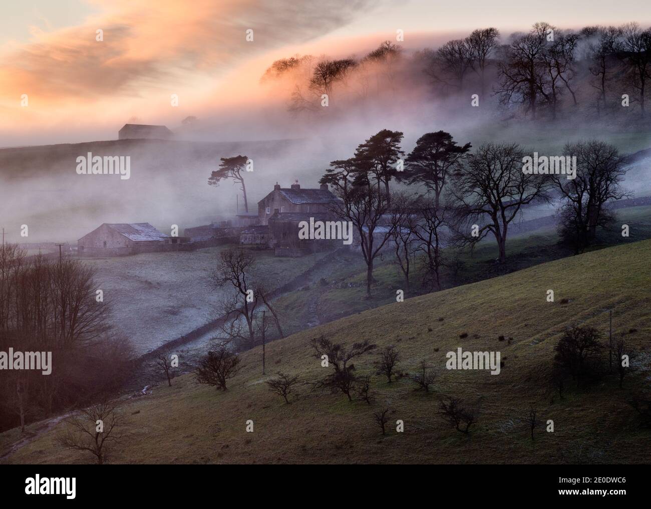 Clima de invierno en el Reino Unido. Mientras se pone el sol, una niebla a última hora de la tarde sube Clapdale envolviendo una granja sobre el pueblo de Clapham en el Parque Nacional de Yorkshire Dales. Crédito: John Bentley/Alamy Live News Foto de stock