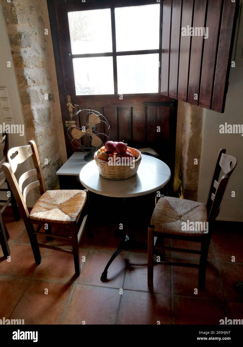 Detalle de una pequeña sala de estar con dos sillas de madera y mesa con una cesta de granadas, casco antiguo de Monemvasia, Grecia Foto de stock