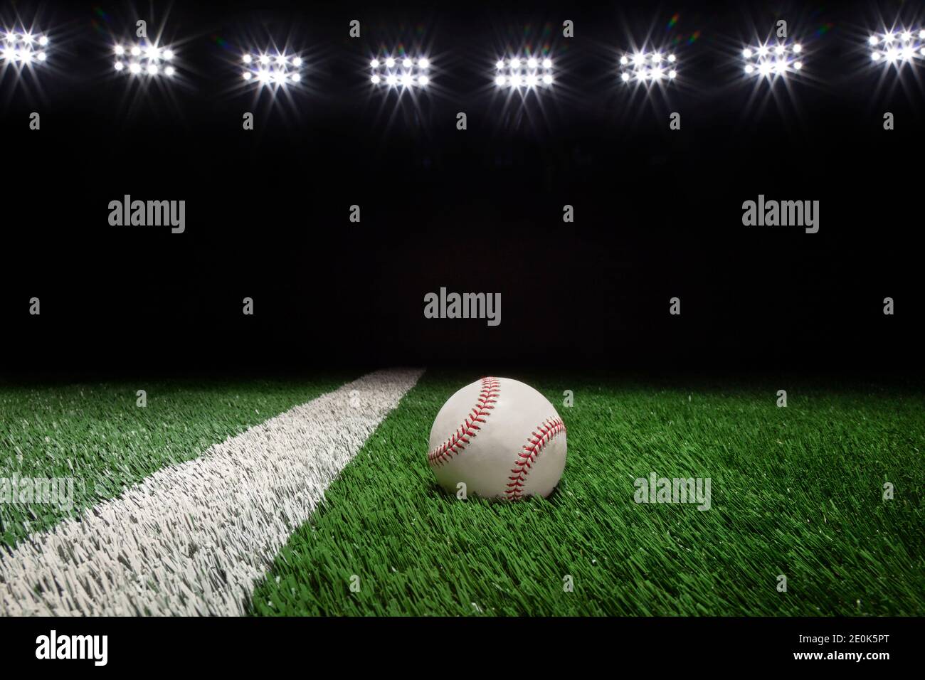 Béisbol en un campo de hierba con rayas y fondo negro bajo las luces Foto de stock