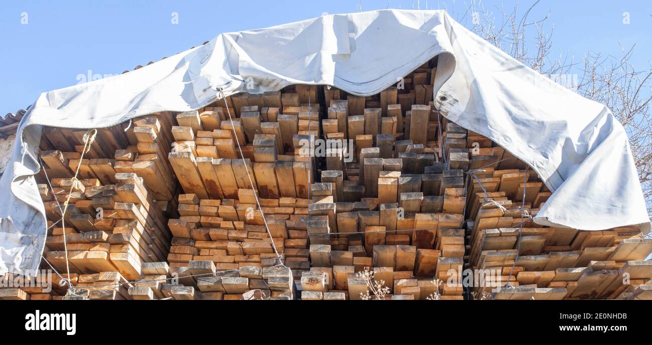 Gran pila de madera protegida por lonas de lona impermeables. Materiales de construcción para la industria de la construcción. Foto de stock