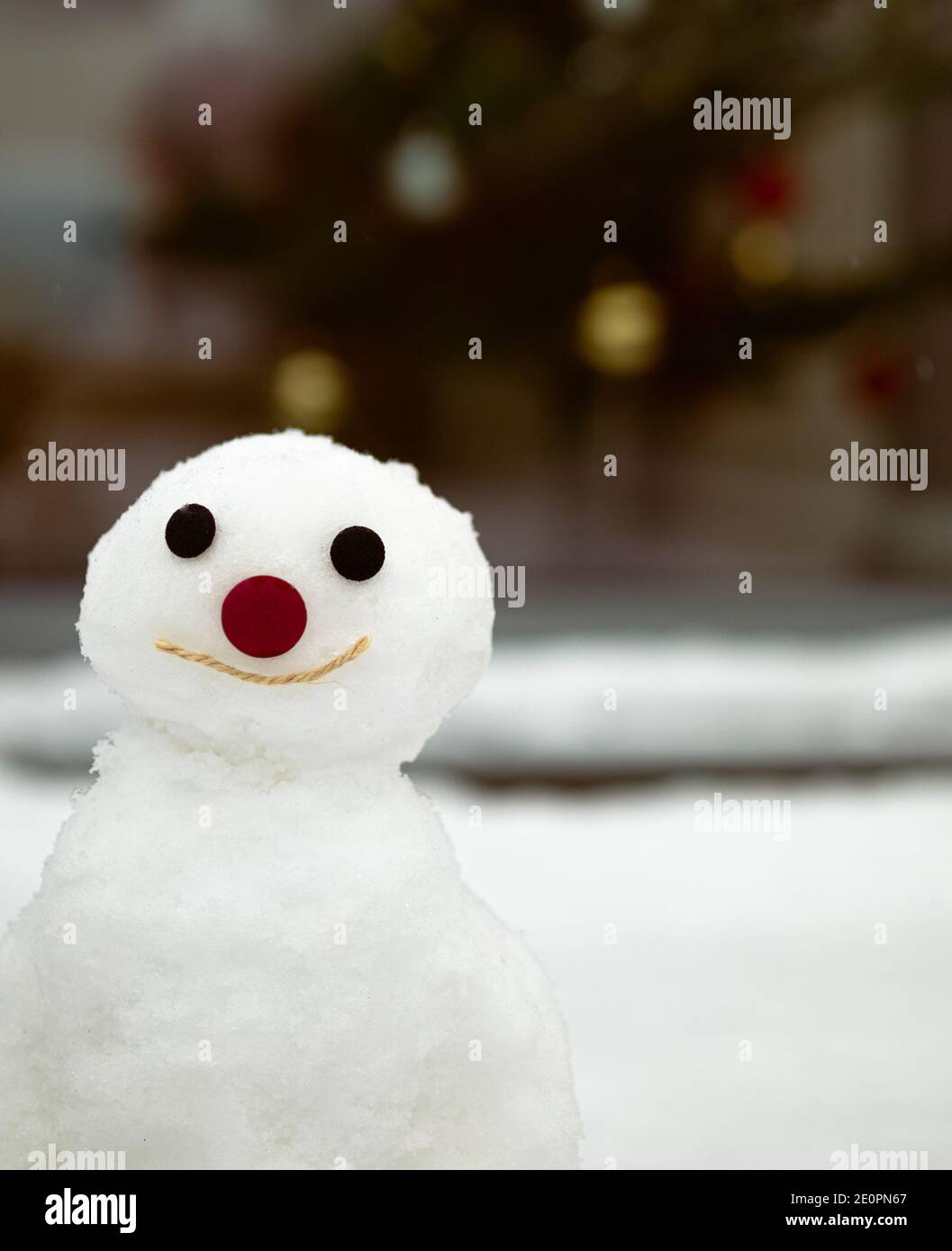 Un muñeco de nieve sonriente cerca con un árbol de Navidad en el fondo Foto de stock
