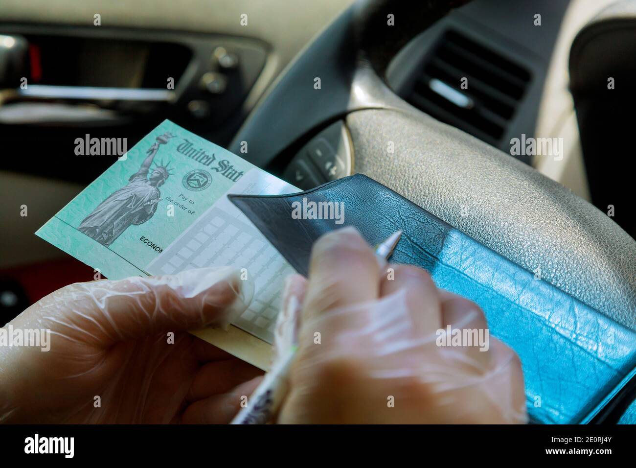 Escribir en cheque en blanco con en el coche con guantes al depositar el estímulo del gobierno cheque con guantes encendido para la seguridad enfoque suave Foto de stock