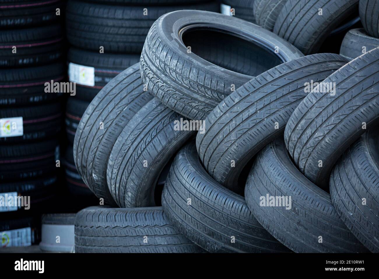 Pila de neumáticos usados sobre un fondo de neumáticos nuevos Foto de stock