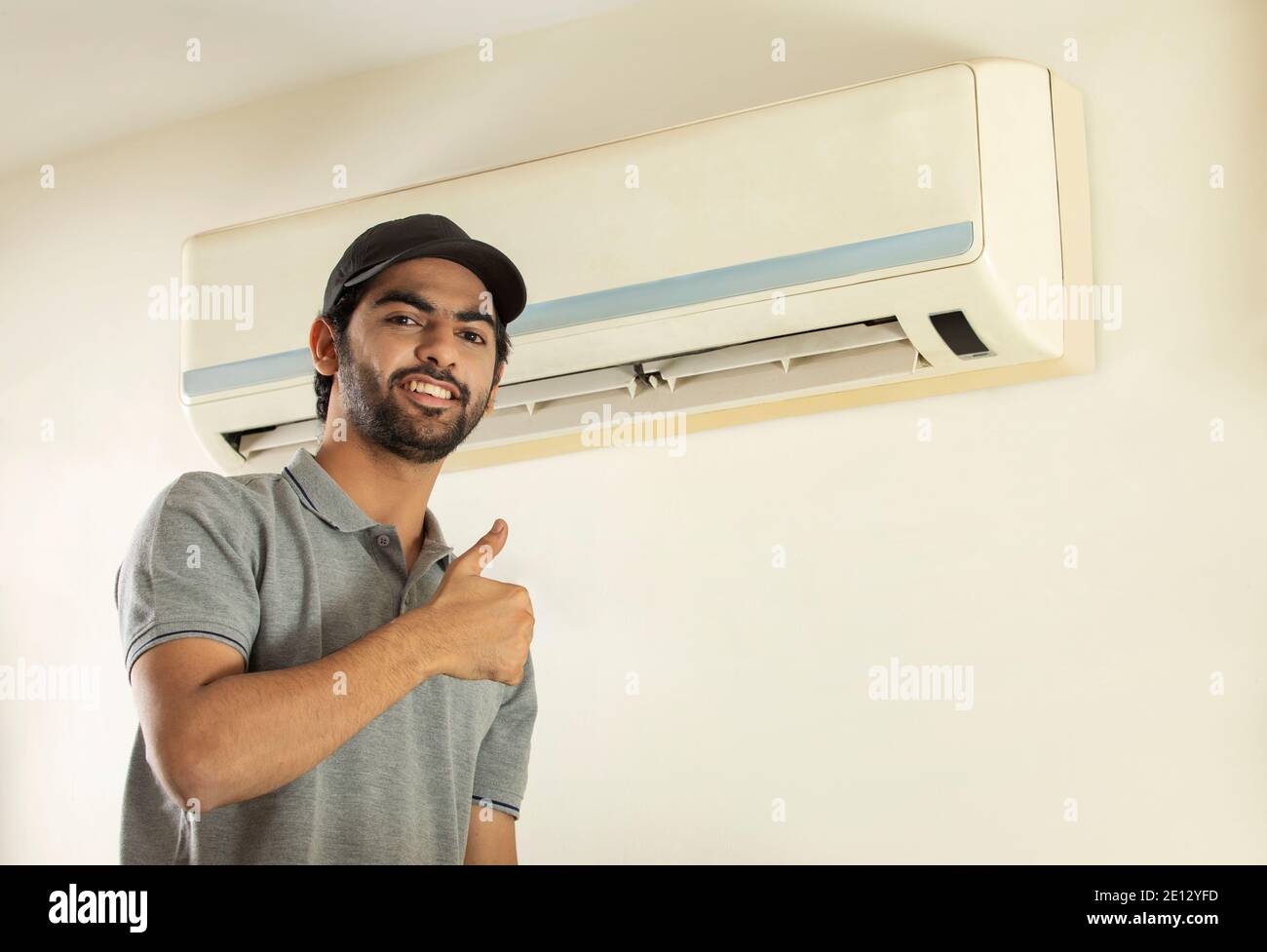 UN JOVEN PROFESIONAL FELIZ SONRIENDO DESPUÉS DE REPARAR EL AIRE ACONDICIONADO Foto de stock