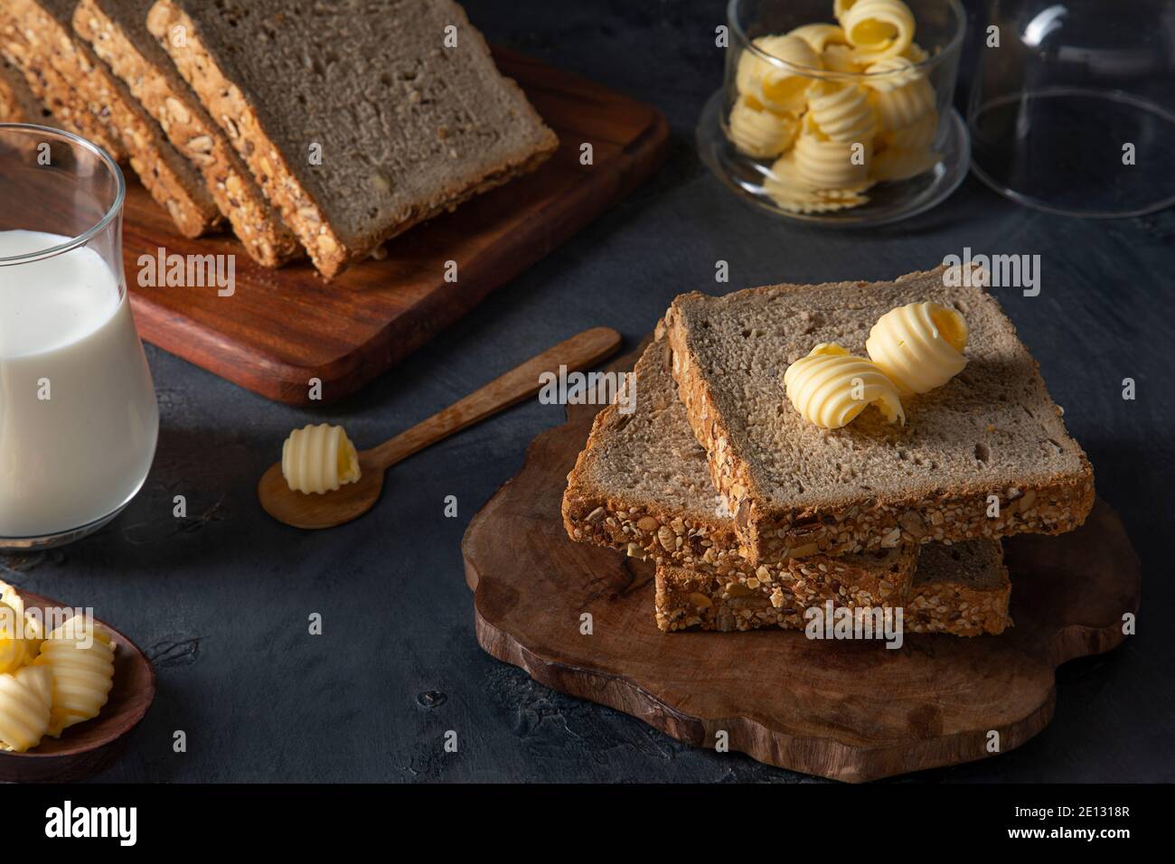 Pan y mantequilla en una mesa negra con un vaso de leche Foto de stock