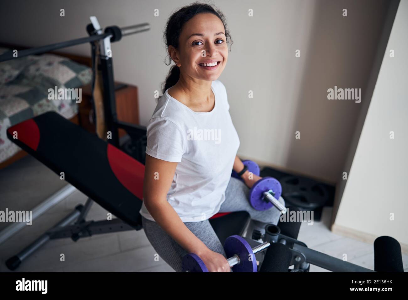 Culturista femenino con pesas sentado en el banco de entrenamiento Foto de stock