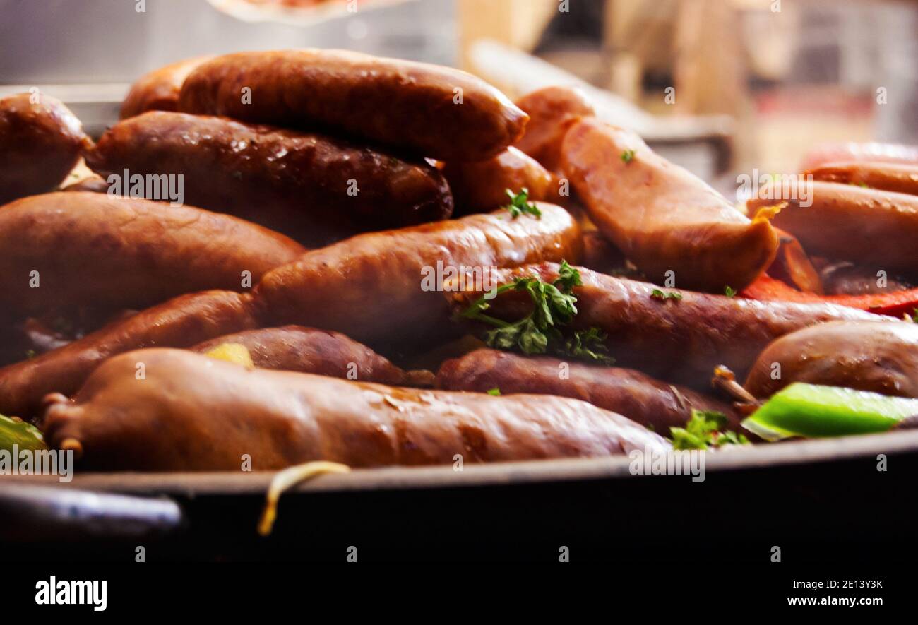 Salchichas tradicionales guisadas calientes con verduras en gran sartén en el mercado de la calle. Primer plano. Aumento del vapor. Mercado de Navidad en París. Foto de stock