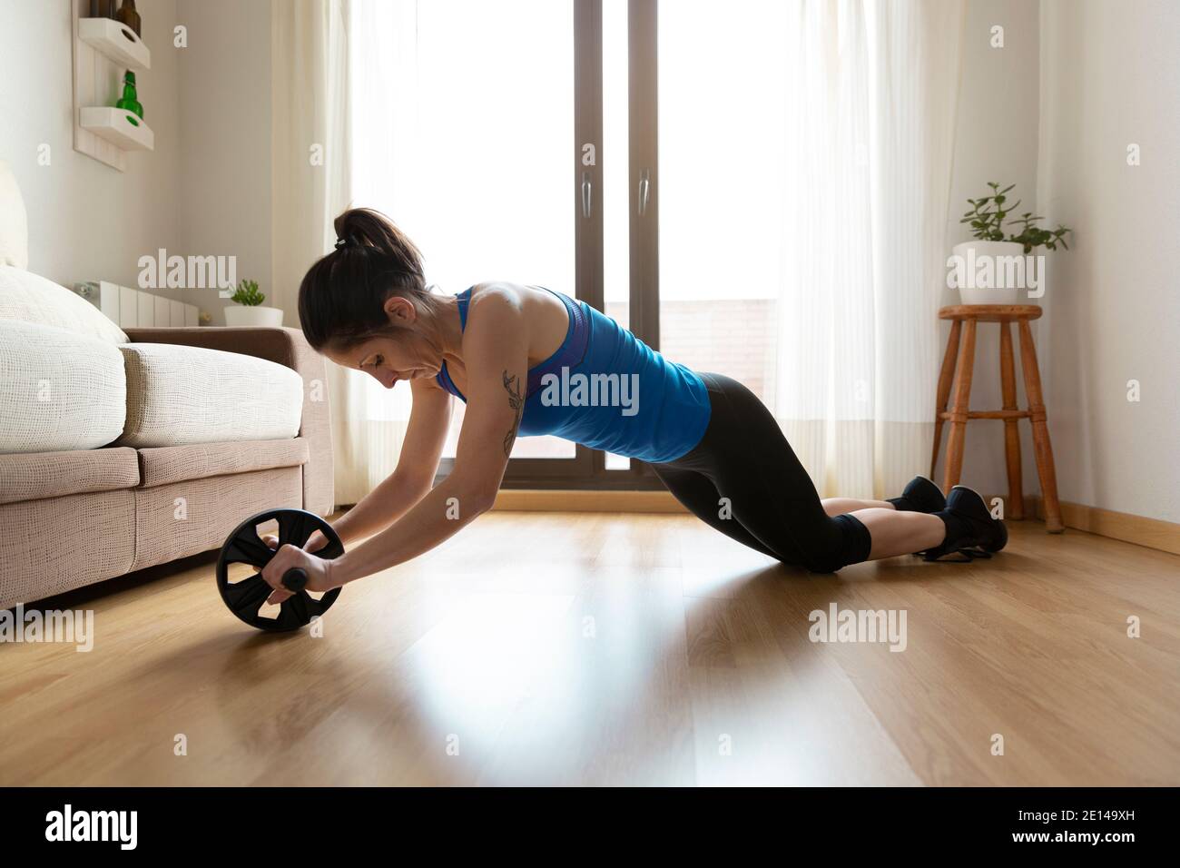 Mujer fortaleciendo su cuerpo mediante el uso de la rueda abdominal. Concepto de deporte en casa. Espacio para texto. Foto de stock