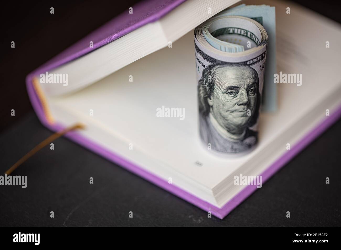 rollo de billetes de 100 dólares en libro violeta Foto de stock