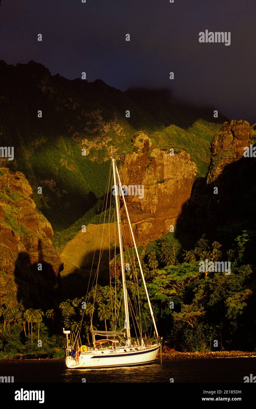 Yacht 'Heron' anchored off the cliffs of Hanavave Bay at sunset, Fatu Hiva, Marquesas, French Polynesia Foto de stock