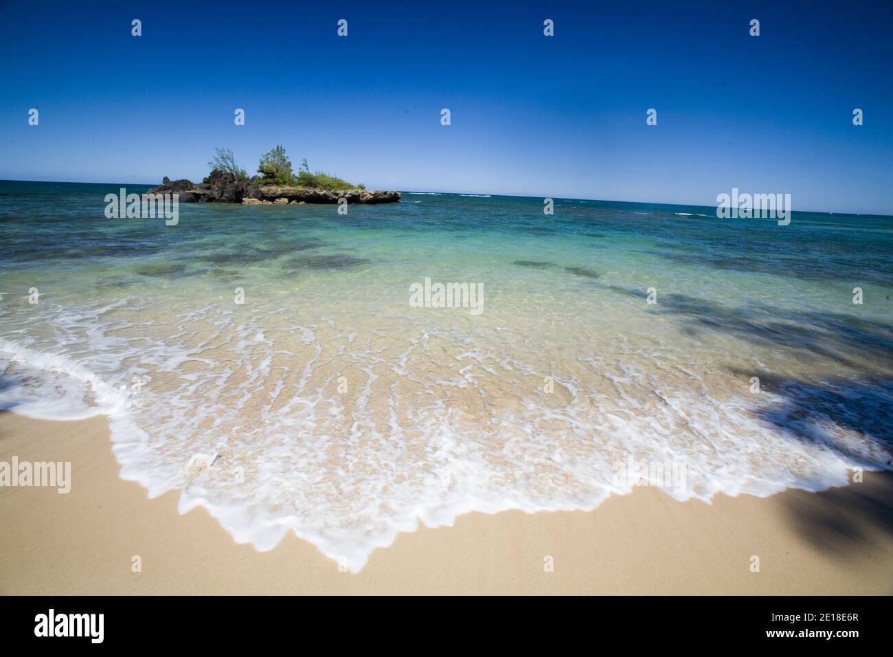 Escena de playa en una playa desierta de la costa norte con un pequeña isla costera en aguas azules claras Foto de stock