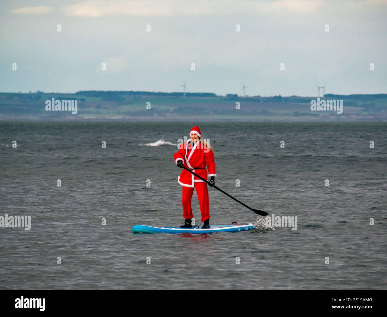 Evento de caridad comunitaria: Paddle boarder en un traje de Santa, Firth of Forth, East Lothian, Escocia, Reino Unido Foto de stock