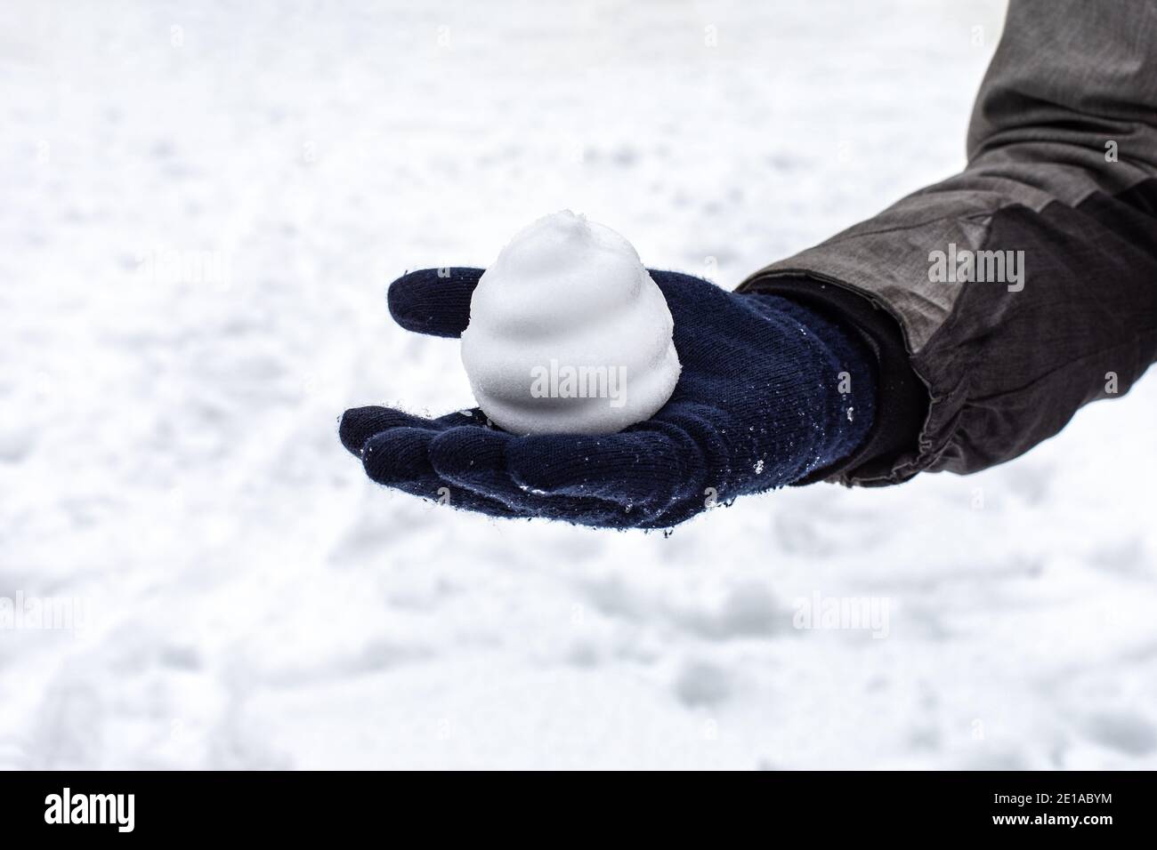 Bola de nieve en forma de pastel en una mano en un mitten, juegos de invierno al aire libre. Temporada humor nieve clima Foto de stock