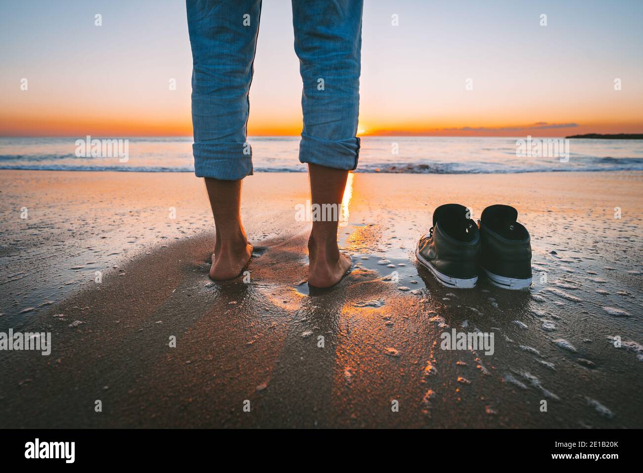 Primer plano de hombre descalzo caminando en la playa de verano al  atardecer. El hombre se deshace de sus zapatos para caminar en el mar  tranquilo. Concepto de relajación y libertad Fotografía