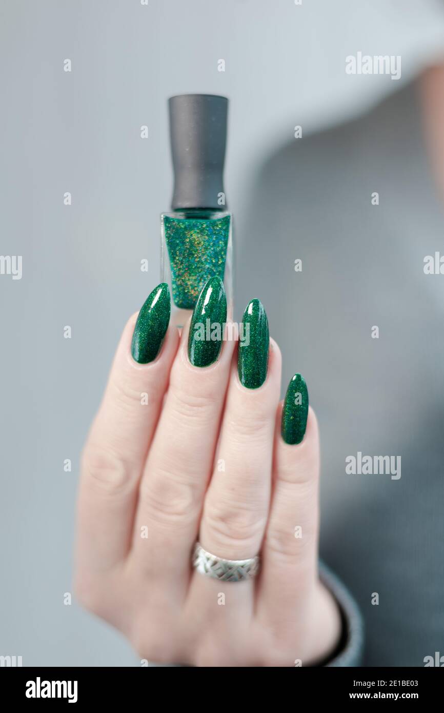 Mano femenina con uñas largas y manicura verde con botellas de esmalte de  uñas Fotografía de stock - Alamy