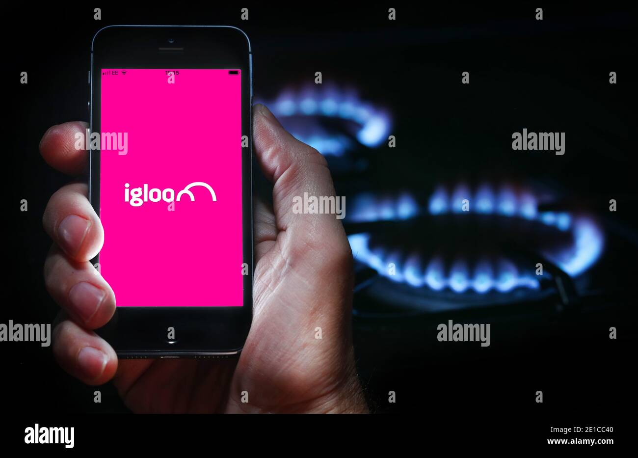 Un hombre mirando el logotipo del sitio web de la empresa de energía IGLOO Energía en su teléfono frente a su gas cocina (solo para uso editorial) Foto de stock