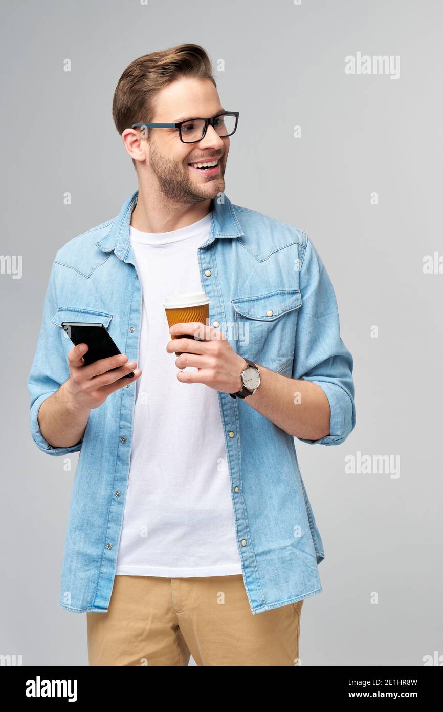 hombre bastante informal en azul jeans camisa sosteniendo su teléfono y  taza de café para ir de pie sobre el gris de estudio antecedentes  Fotografía de stock - Alamy