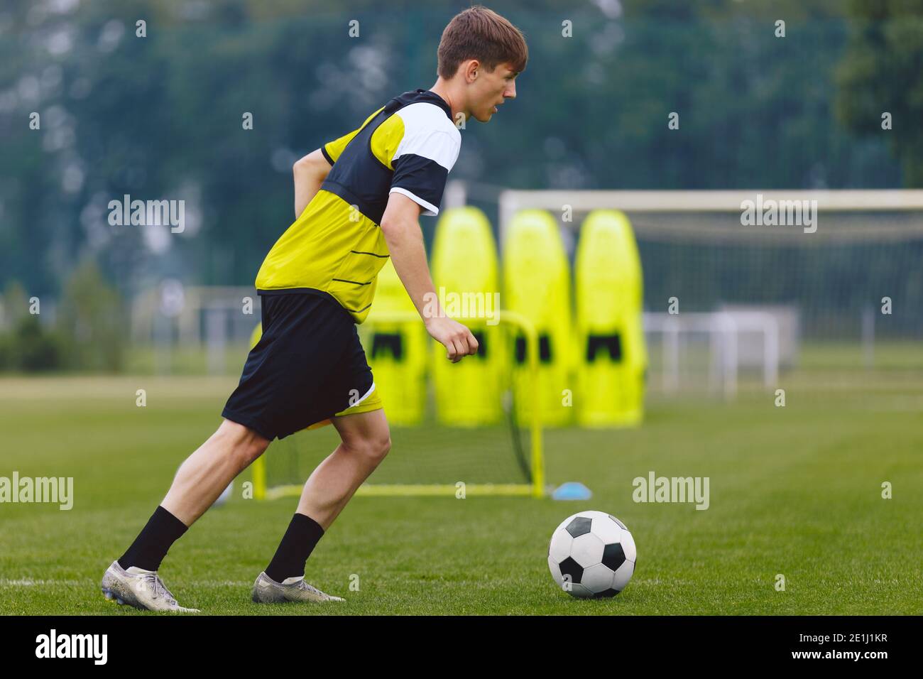 Boys Running Soccer Ball en el lugar de entrenamiento. Deportista joven practicando fútbol en campo de hierba. Fútbol Wall Mannequin set y meta de entrenamiento en la espalda Foto de stock