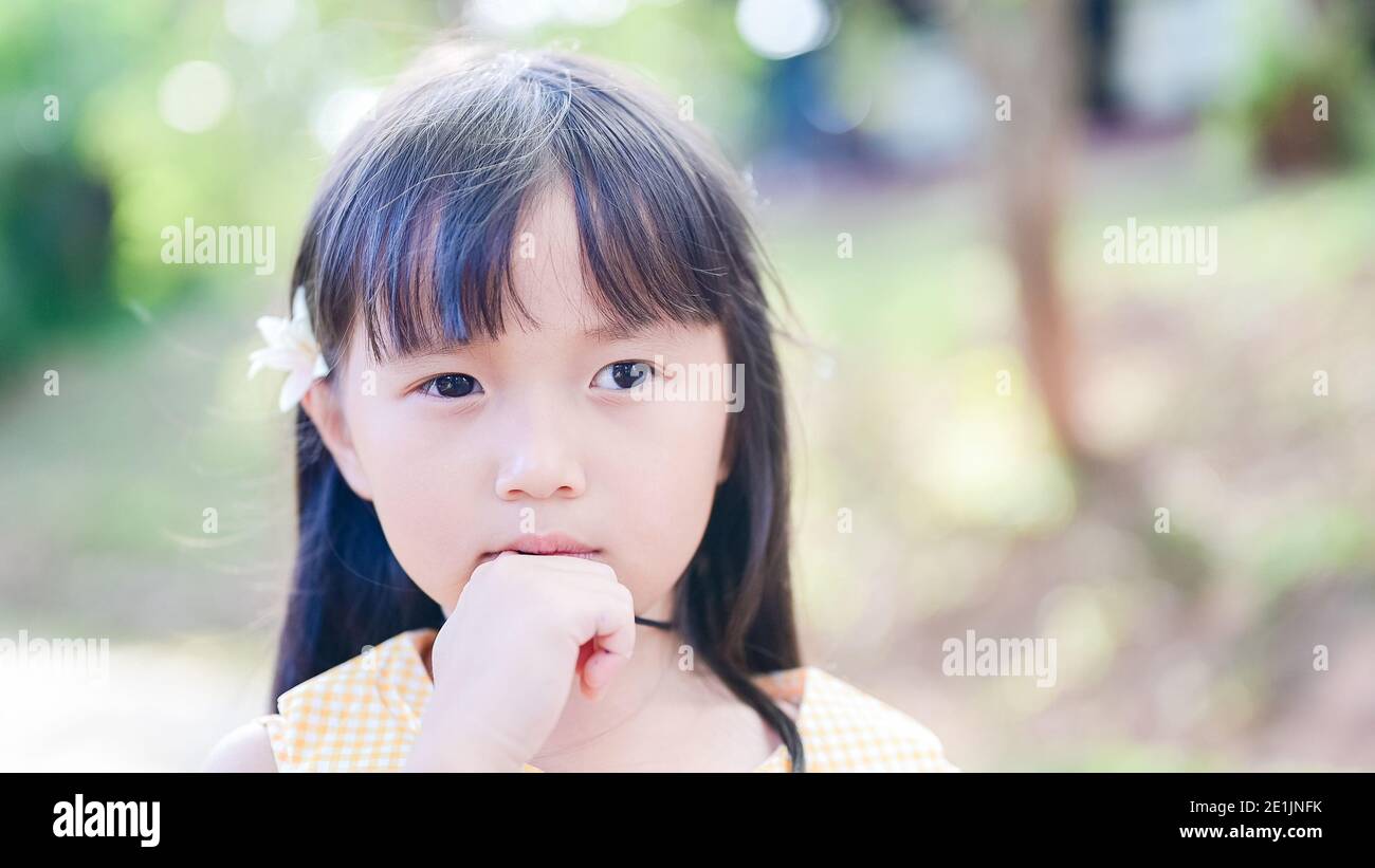 Cute niña asiática Tuck una flor blanca en su y mira la cámara Foto de stock