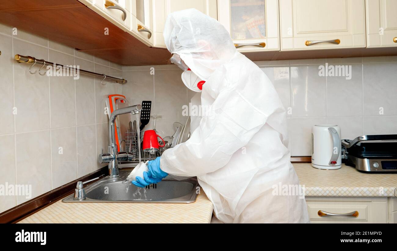 Ama de casa con miedo del coronavirus y covid-19 usando traje de protección  médica y lavar los platos con mascarilla en la cocina Fotografía de stock -  Alamy