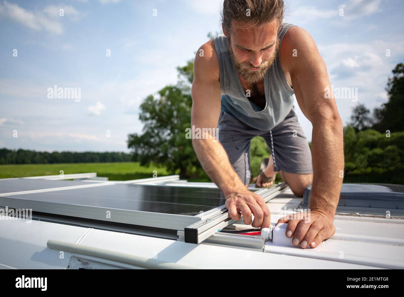 Hombre conectando los paneles solares en la parte superior de un campista van Foto de stock