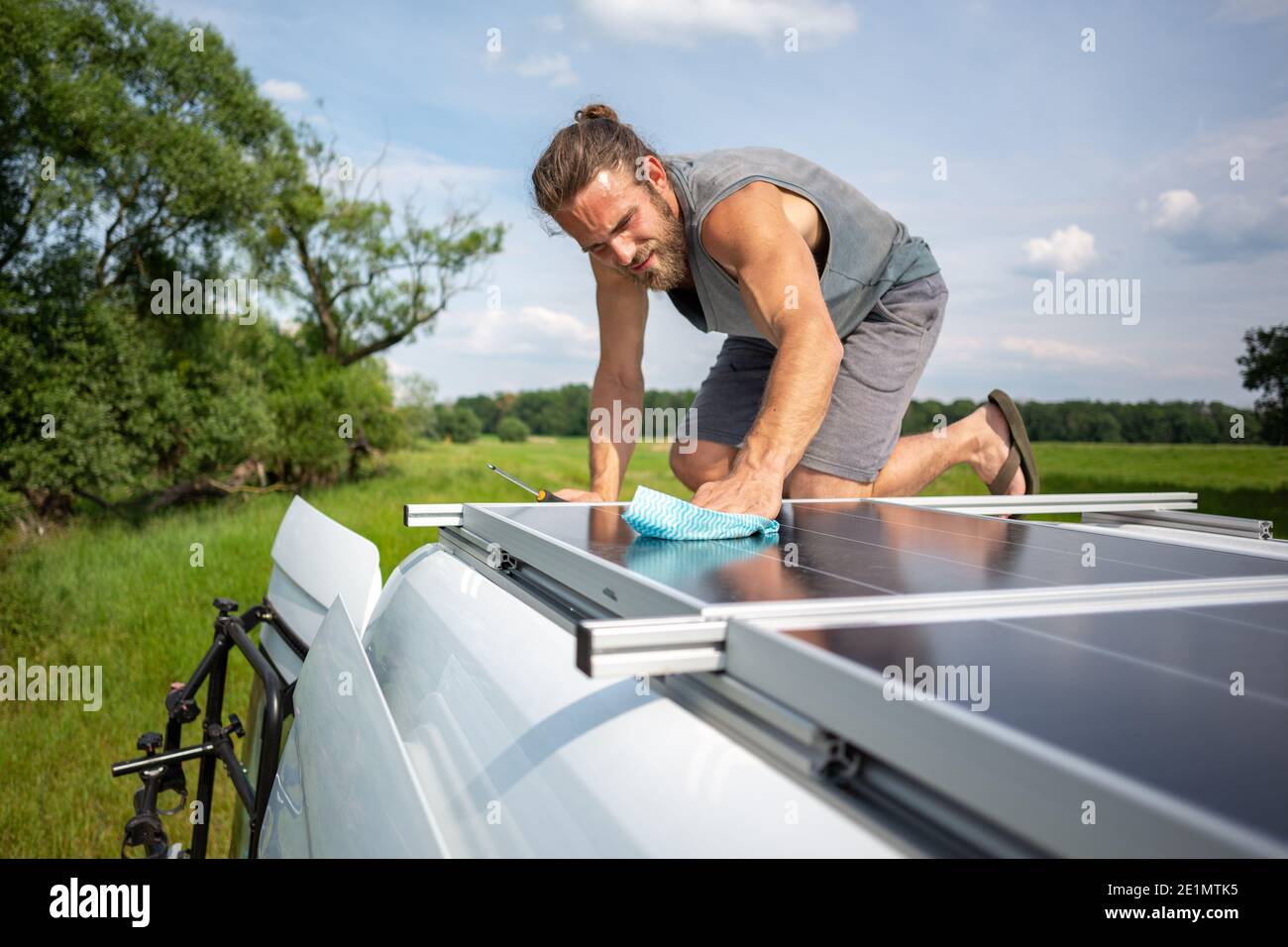 Hombre limpiando un panel solar en la parte superior de una caravana Foto de stock