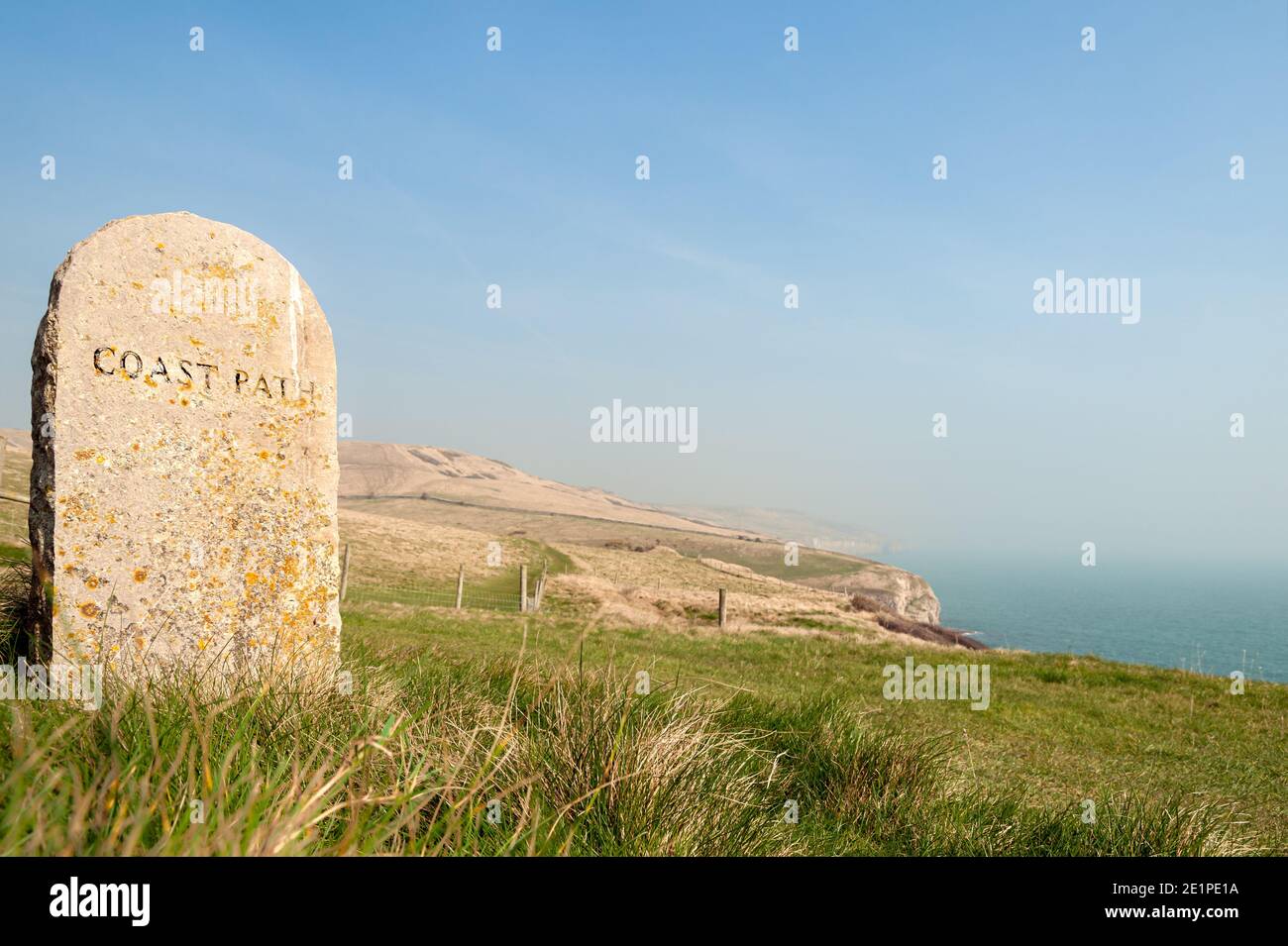 Viejo marcador de piedra con el texto de camino de la costa tallado y descolorido vista del mar y acantilados en el fondo para su uso como un fondo Foto de stock