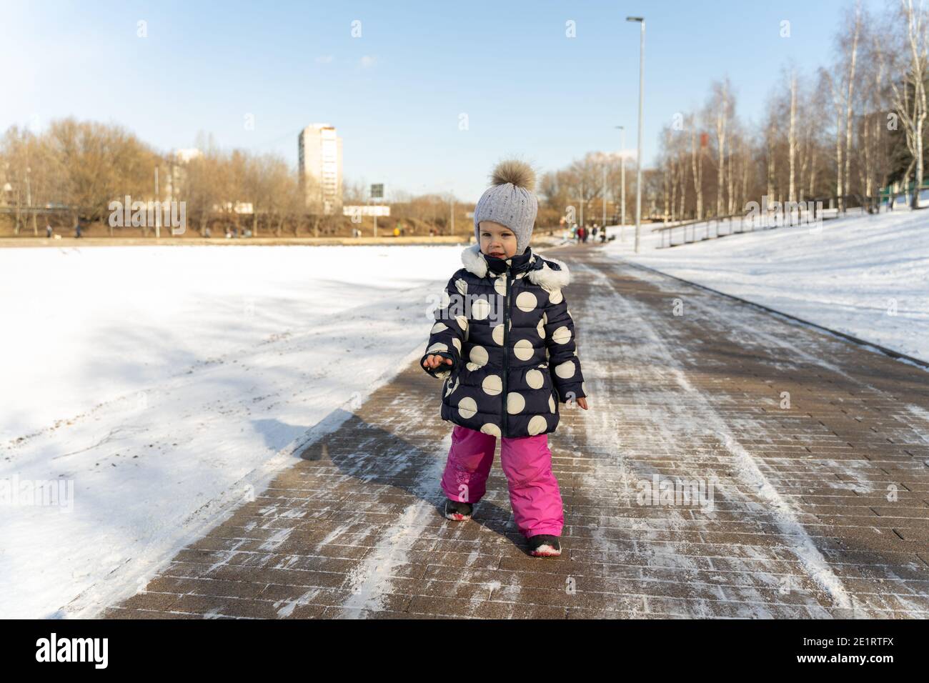 un niño de 3-4 años camina por el amplio dique de un estanque congelado en invierno en un día soleado Foto de stock