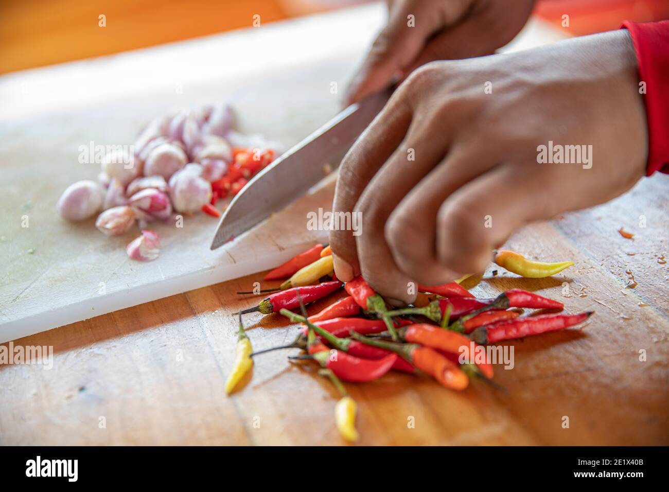 primer plano de una mano cortando cebolla blanca y chile pimienta en un tablero de la cocina con un cuchillo Foto de stock
