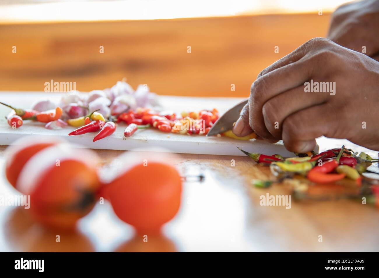 primer plano de una mano cortando cebolla blanca y chile pimienta en un tablero de la cocina con un cuchillo Foto de stock