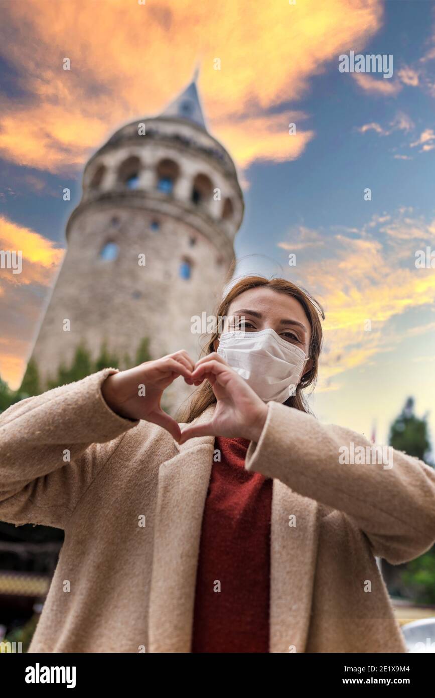 Sinewi Panadería frecuentemente Hermosa chica con máscara médica protectora y ropa de moda hace forma de  corazón con vistas a la Torre de Gálata Fotografía de stock - Alamy