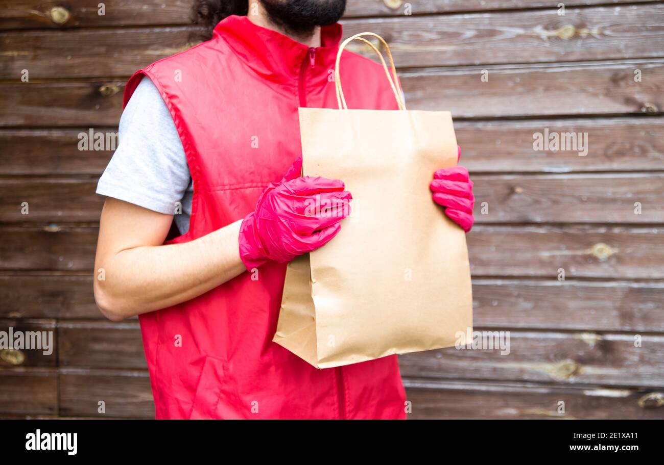 Concepto de entrega y compra en línea. Courier, el hombre de la entrega en  uniforme rojo y guantes entrega con seguridad las compras en línea en bolsas  de papel de crandt a