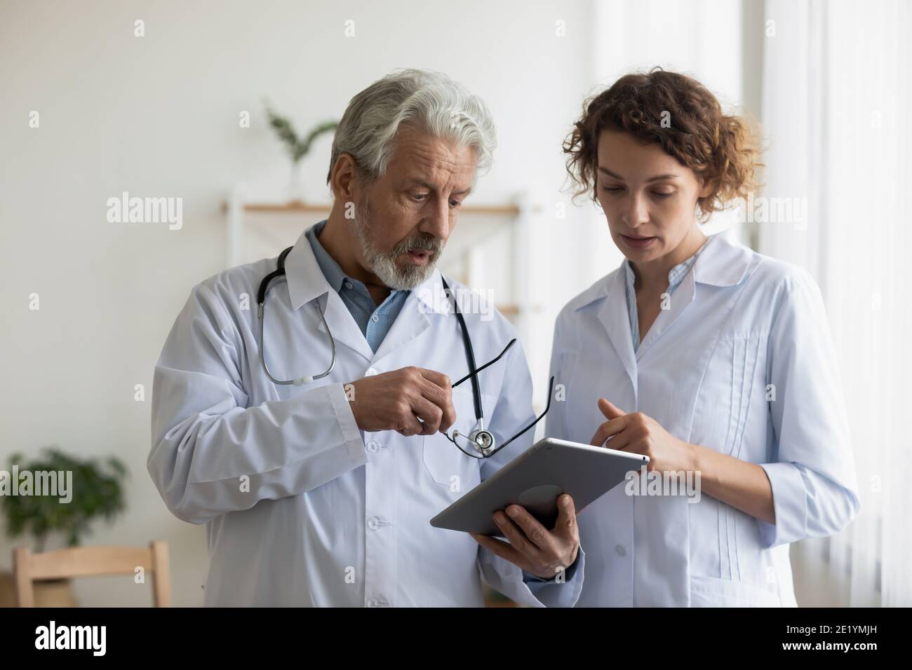 Médico anciano serio que discute los resultados de la prueba con un colega joven. Foto de stock