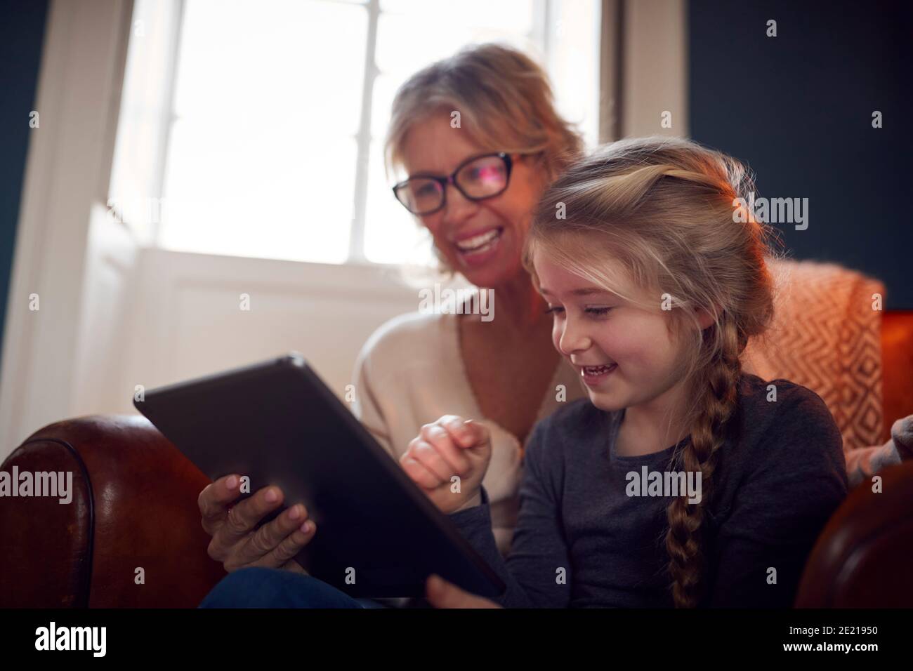 Nieta con abuela en silla mirando a la tableta digital en Casa juntos Foto de stock