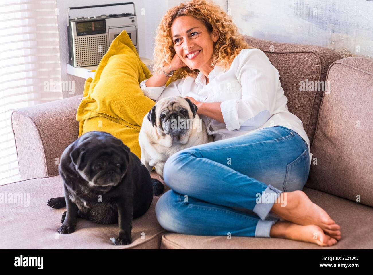Retrato de joven adulto alegre hermosa mujer con dos perros pug sentado y relajándose en el sofá en casa - concepto de propietario de animales y diario real l Foto de stock