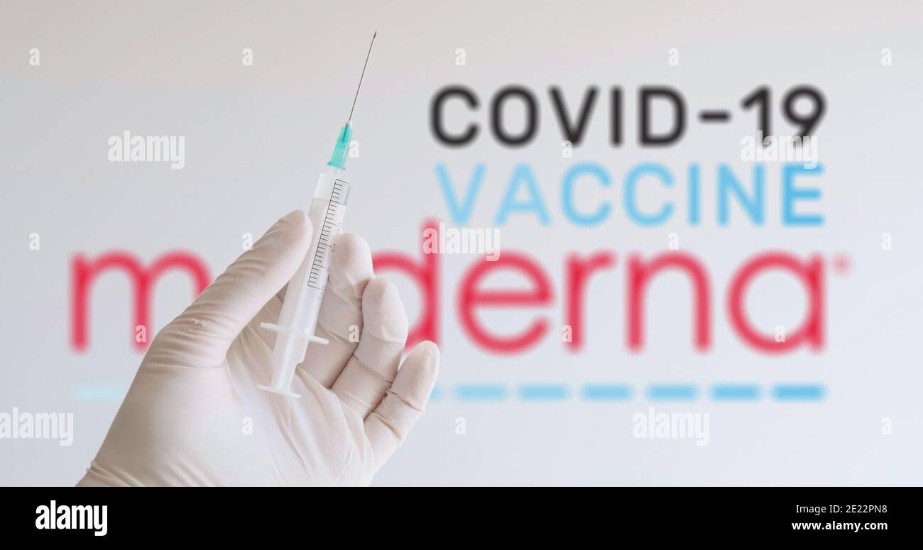 Una mano con un guante que sostiene la jeringa delante del logo de moderna, una de las empresas que producen una vacuna Covid-19 (Coronavirus). Viena, Austria - Enero Foto de stock