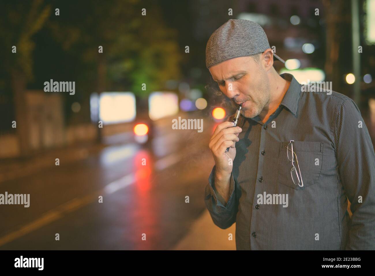 Hombre maduro que fuma cigarrillos electrónicos en las calles por la noche en blanco y negro Foto de stock